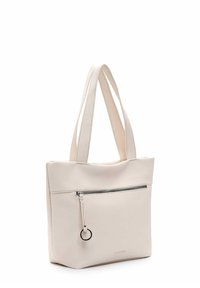 Sac tote en cuir blanc avec deux poignées longues, une poche zippée à l'avant et un accent en matériel circulaire. Texture lisse et design minimaliste.