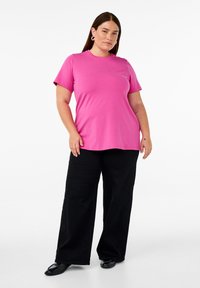 Rosa Baumwoll-T-Shirt mit klassischem Rundhals, kurzen Ärmeln und lockerer Passform, kombiniert mit weiten schwarzen Hosen und schwarzen Schuhen.