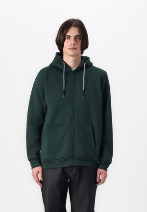 Grüne Zip-Hoodie mit Kapuze mit Kordelzug, zwei frontalen Taschen, geripptem Saum und Bündchen, aus weichem Material. Jeans sind darunter sichtbar.