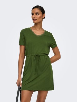 Woman wearing a short-sleeve olive green dress with a drawstring waist and V-neck, holding a black handbag with her left hand.