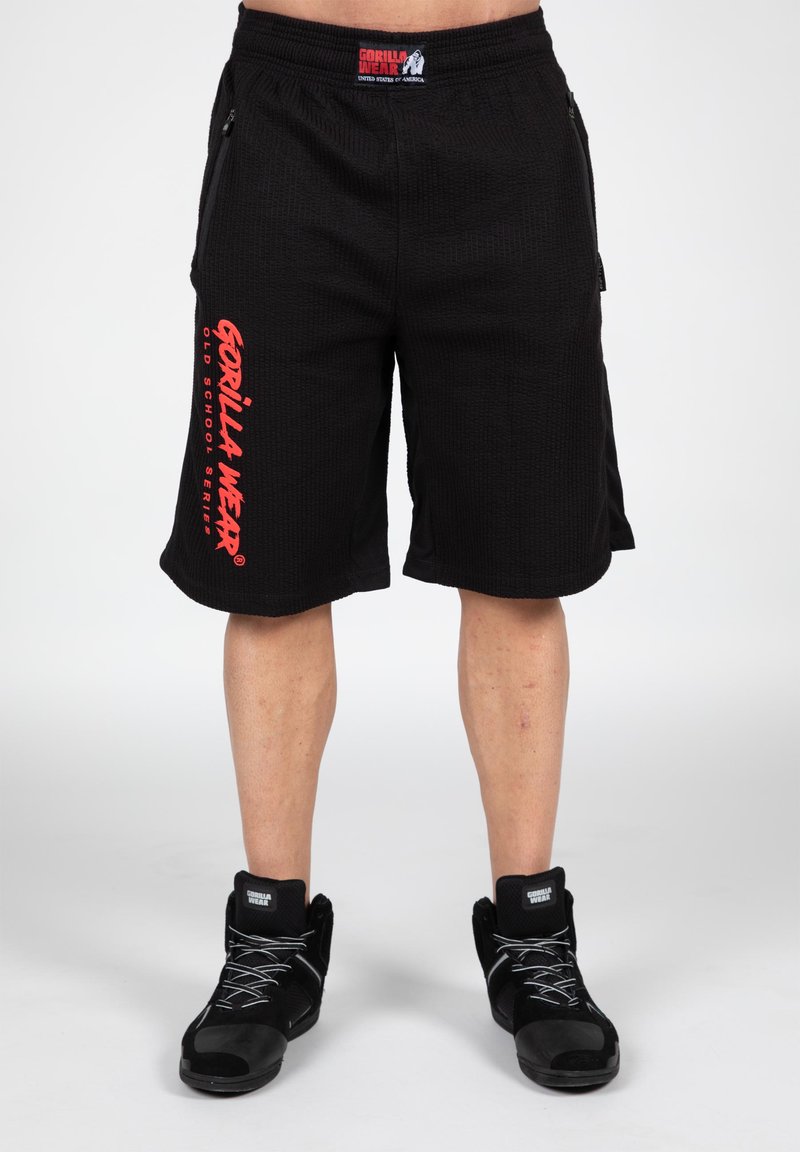 Black athletic shorts with a textured fabric, side pockets, and red "GORILLA WEAR" logo on the left leg. Paired with black high-top shoes.