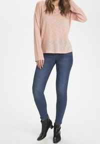 Różowa bluzka z długim rękawem o luźnym kroju, zestawiona z dopasowanymi, ciemnoniebieskimi dżinsami oraz czarnymi botkami za kostkę z ostrym noskiem i słupkowym obcasem.