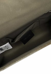 Interno di una borsa tote in tela di colore verde oliva, con una texture liscia, una tasca e un'etichetta nera; include un'etichetta per la cura e un codice a barre.