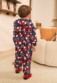 Fleecowy kombinezon w granatowej kolorystyce, z czerwonymi motywami Spidermana i białymi akcentami, połączony z czerwonymi butami wsuwanymi, widoczny od tyłu.
