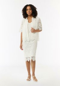 Weißes Spitzen-Dreiteiliges Outfit bestehend aus einer kurzärmeligen Jacke, einem schichtartigen Oberteil und einem knielangen Rock mit gewelltem Saum und Blumenmustern.