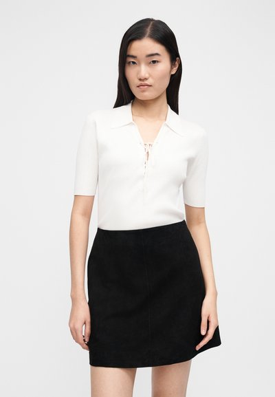 White ribbed short-sleeve top with a collar and lace-up detail, paired with a black suede mini skirt, featuring a straight cut and soft texture.