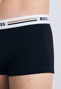 Čierne bavlnené boxerky s bielym pásom na kontrastný vzor a s potlačeným názvom značky "BOSS" v čiernej farbe.