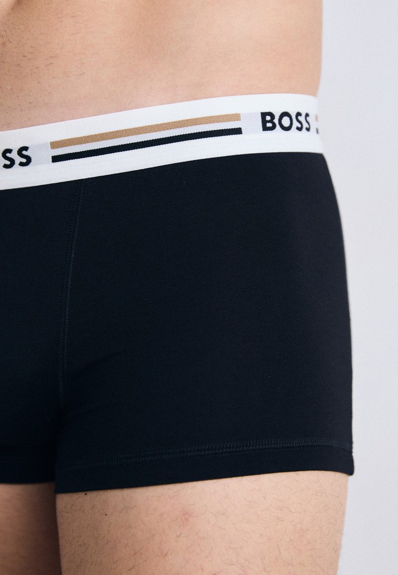 Czarne bawełniane bokserki z białą gumką w kontrastowym wzorze pasków oraz nazwą marki "BOSS" wydrukowaną na czarno.