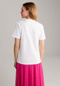 Witte T-shirt met korte mouwen van katoen, met een eenvoudige ronde hals en een rechte zoom, gecombineerd met een vloeiende roze rok.