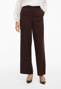 Ruske leve široke hlače z gladkim materialom, prilagojene silhuete in diskretnimi stranskimi žepi, v kombinaciji z ostrimi črnimi čevlji.