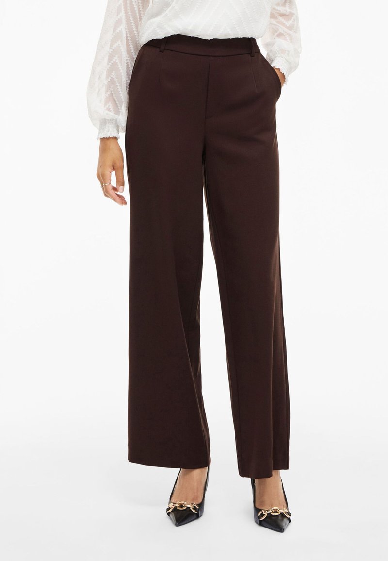 Ruske leve široke hlače z gladkim materialom, prilagojene silhuete in diskretnimi stranskimi žepi, v kombinaciji z ostrimi črnimi čevlji.