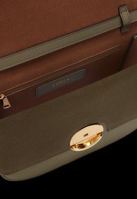 Hnědý semišový interiér s zelenou koženou základnou. Obsahuje zlaté kruhové zapínání a zipovou kapsu s modrou etiketou s embosovaným nápisem "Furla."