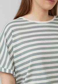 Gestreiftes T-Shirt in Hellgrün und Weiß, kurze Ärmel, runder Halsausschnitt, aus weichem Baumwollgewebe mit lockerer Passform und sichtbaren Nähten.