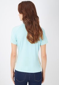 Camisa de manga corta azul claro con cuello redondo. Presenta una forma ajustada y paneles laterales en contraste color crema. Textura suave y lisa.