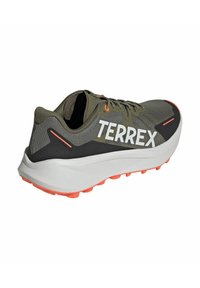 Zapatilla de running en gris y negro con un logo blanco de "TERREX", que presenta acentos naranjas, un upper texturizado y una suela blanca gruesa con tacos de tracción.