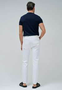 Camisa de manga corta navy, jeans blancos y sandalias negras. Tela suave, diseño ajustado y detalles de costura visibles en los jeans.