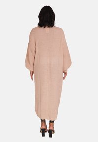 Lång, stickad cardigan i mjuk rosa, med överdimensionerade ärmar och lös passform, med ett texturerat mönster och längd som går nedanför knäna.