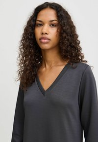 Langärmliges graues V-Ausschnittoberteil aus einem weichen, glatten Stoff mit minimalistischem Design und dezentem Glanz, ausgestattet mit einem klassischen Schnitt und ohne Muster.