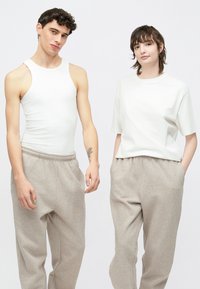 Λευκό αμάνικο τοπ συνδυασμένο με ανοιχτό γκρι φόρμες αριστερά· λευκό μπλουζάκι με ανοιχτό γκρι φόρμες δεξιά. Καθημερινά ρούχα αθλητικού στυλ.