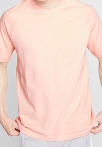 Camiseta de manga corta color rosa claro con cuello redondo y mangas raglán, hecha de un tejido suave; diseño sencillo sin patrones ni elementos metálicos.