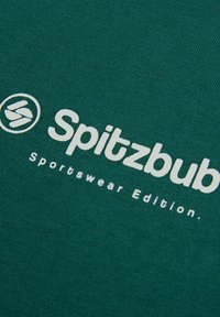 Grüner Stoff mit weißem Text: "Spitzbub Sportswear Edition" und einem kreisförmigen Logo, das ein lässiges Sportbekleidungs-T-Shirt-Design anzeigt.
