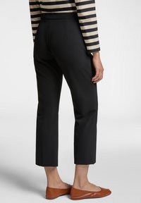 Pantaloni neri cropped con una texture liscia, caratterizzati da un design pulito e una vestibilità sartoriale, abbinati a ballerine marroni.