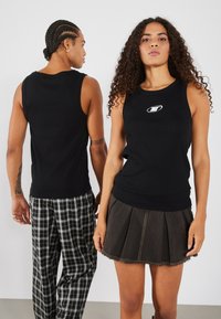 Débardeur noir à côtes avec un col rond et un petit logo sur la poitrine, associé à une jupe en denim foncé plissée et un pantalon à carreaux.