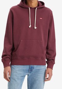 Vínový mikina s klokaní kapsou a šňůrkami. Obsahuje malé červené logo na hrudi. Měkký materiál, žebrované manžety a lem.