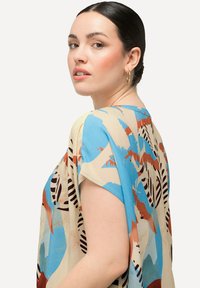 Blusa a fantasia con una combinazione di colori blu, arancione e marrone, caratterizzata da forme astratte. Tessuto morbido con maniche corte e una vestibilità rilassata.
