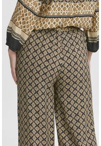 Pantalons larges avec une base foncée et un motif géométrique doré et noir. Tissu doux avec une taille élastique et un détail en bouton au dos.