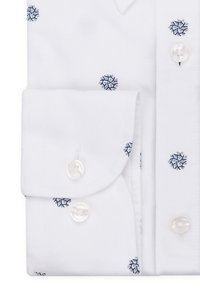 Biała koszula z niebieskimi haftowanymi wzorami płatków śniegu, z kołnierzykiem zapinanym na guziki, zaokrąglonymi mankietami i guziki przypominającymi perły. Gładka faktura materiału.