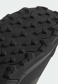 Schwarze Gummisohle mit robustem, multidirektionalem Profil für verbesserten Halt und den Einsatz im Freien.