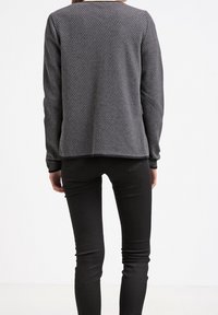 Šedé dlouhé rukávy top s texturovaným šestiúhelníkovým vzorem, kulatým výstřihem a volným střihem. Nosit na černé upevněné kalhoty.