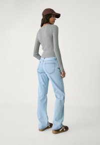 Gray ribbed sweater with a fitted waist, paired with light blue straight-leg jeans and brown shoes featuring white accents and a cap.