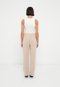 Λευκό αμάνικο τοπ συνδυασμένο με μπεζ παντελόνια φαρδιάς γραμμής. Η στολή διαθέτει λεία υφή και ελαστική μέση. Μαύρα αθλητικά παπούτσια ολοκληρώνουν την εμφάνιση.