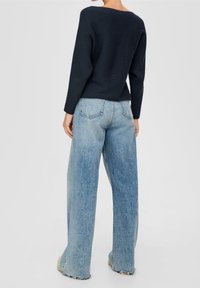 Suéter de punto acanalado en color navy con mangas anchas, combinado con jeans de pierna ancha en un tono azul claro, que presentan un acabado desgastado y dobladillos deshilachados.