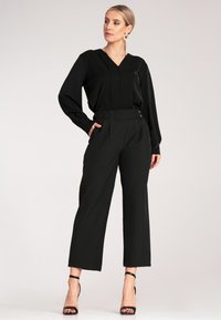 Czarna bluzka z dekoltem w serek i długimi rękawami, zestawiona z czarnymi szerokimi spodniami o wysokim stanie. Posiada akcenty w postaci guzików oraz gładką fakturę.