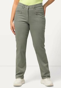 Ljusgröna byxor med en slät textur, två fickor med dragkedja framtill och en figurnära design. Stylar med beige sneakers.