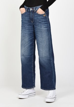 Weite Denim-Jeans in mittlerem Waschung mit einer verwaschenen Textur. Verfügt über Fronttaschen und einen Knopfverschluss. Kombiniert mit weißen High-Top-Sneakern.