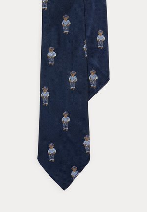 Krawat w kolorze granatowym z powtarzającymi się haftowanymi postaciami niedźwiedzi w czapce z daszkiem, w paskowanej koszuli i dżinsach.