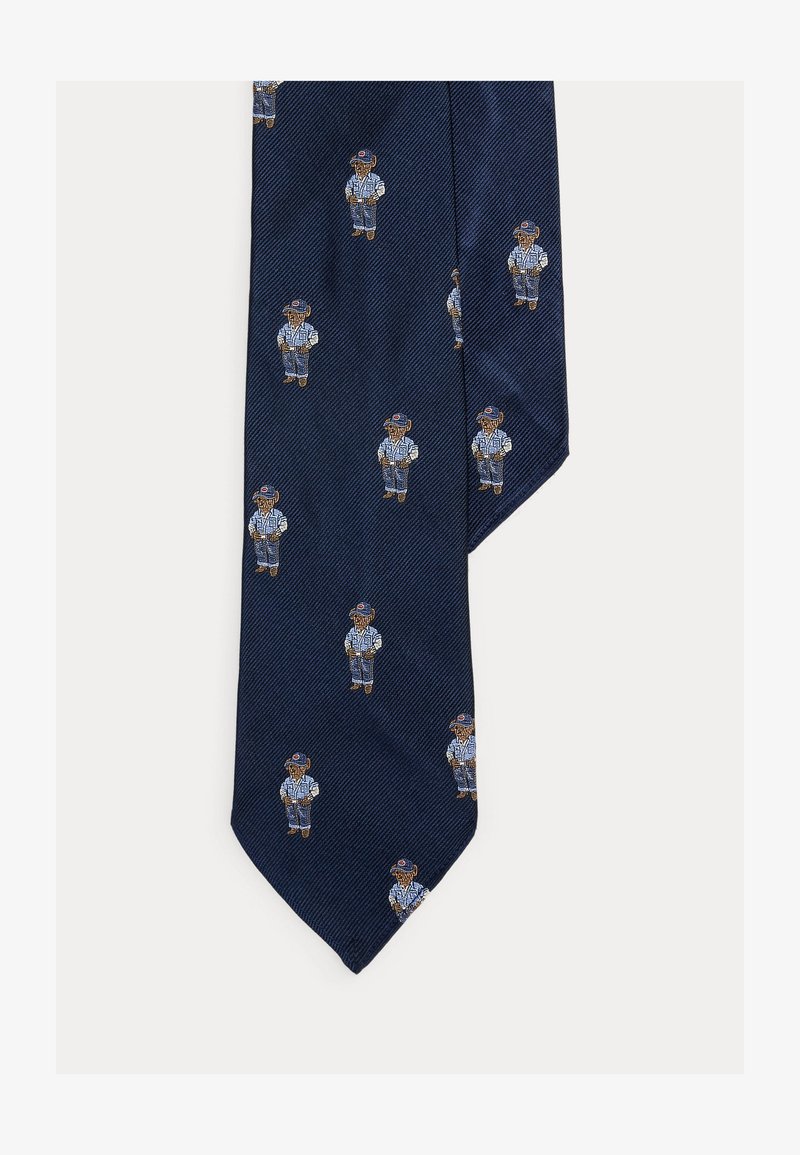 Γραβάτα σε ναυτικό μπλε χρώμα με επαναλαμβανόμενα κεντημένα σχέδια αρκούδων που φοράνε καπέλο μπέιζμπολ, ριγέ πουκάμισο και τζιν παντελόνι.