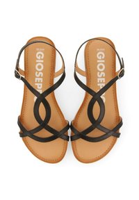 Sandalias de cuero negro con correas entrelazadas y una plantilla marrón. Cuentan con una correa ajustable en el tobillo y una suela plana.