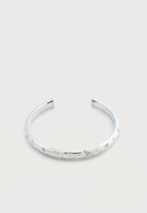 Brazalete abierto de plata con grabados de luna y estrellas en una superficie lisa y pulida sobre un fondo blanco.