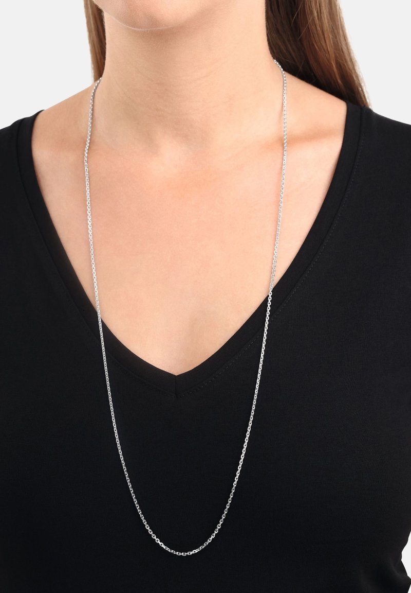 Collar de plata con una delicada cadena alargada, llevado sobre una blusa negra de escote en V, que enfatiza el diseño elegante y el acabado metálico.