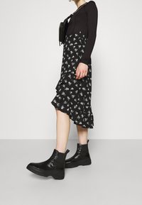 Musta pitkähihaiseen paita yhdistetty mustaan kukkakuosisia mekkoon, jossa on röyhelöreuna. Yhdistetty massiivisiin mustiin nilkkureihin.