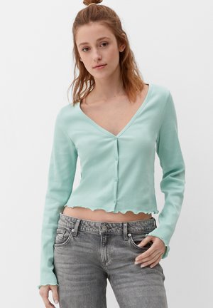 Mintgroene geribde cardigan met lange mouwen, een V-halslijn en golvende randjes. Voor te sluiten met vijf knopen aan de voorkant. Draagt met grijze jeans.