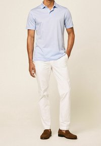 Polo bleu clair à manches courtes, associé à un pantalon blanc et à des mocassins marron. Le tissu semble lisse et léger.