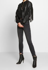 Czarna skórzana kurtka z frędzlami o dopasowanym kroju, zestawiona z ciemnymi obcisłymi dżinsami i botkami na wysokim obcasie. Gładkie tekstury i detale.