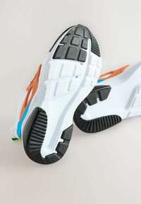 Hvide atletik sko med farvede accenter i orange, blå og grøn. Tykkede, strukturerede gummisåler med unikke dækmønstre og detaljer.