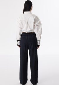Chemise blanche à boutons avec des manches bouffantes et des poignets noirs contrastants, associée à un pantalon large bleu marine doté d'une ceinture élastique.